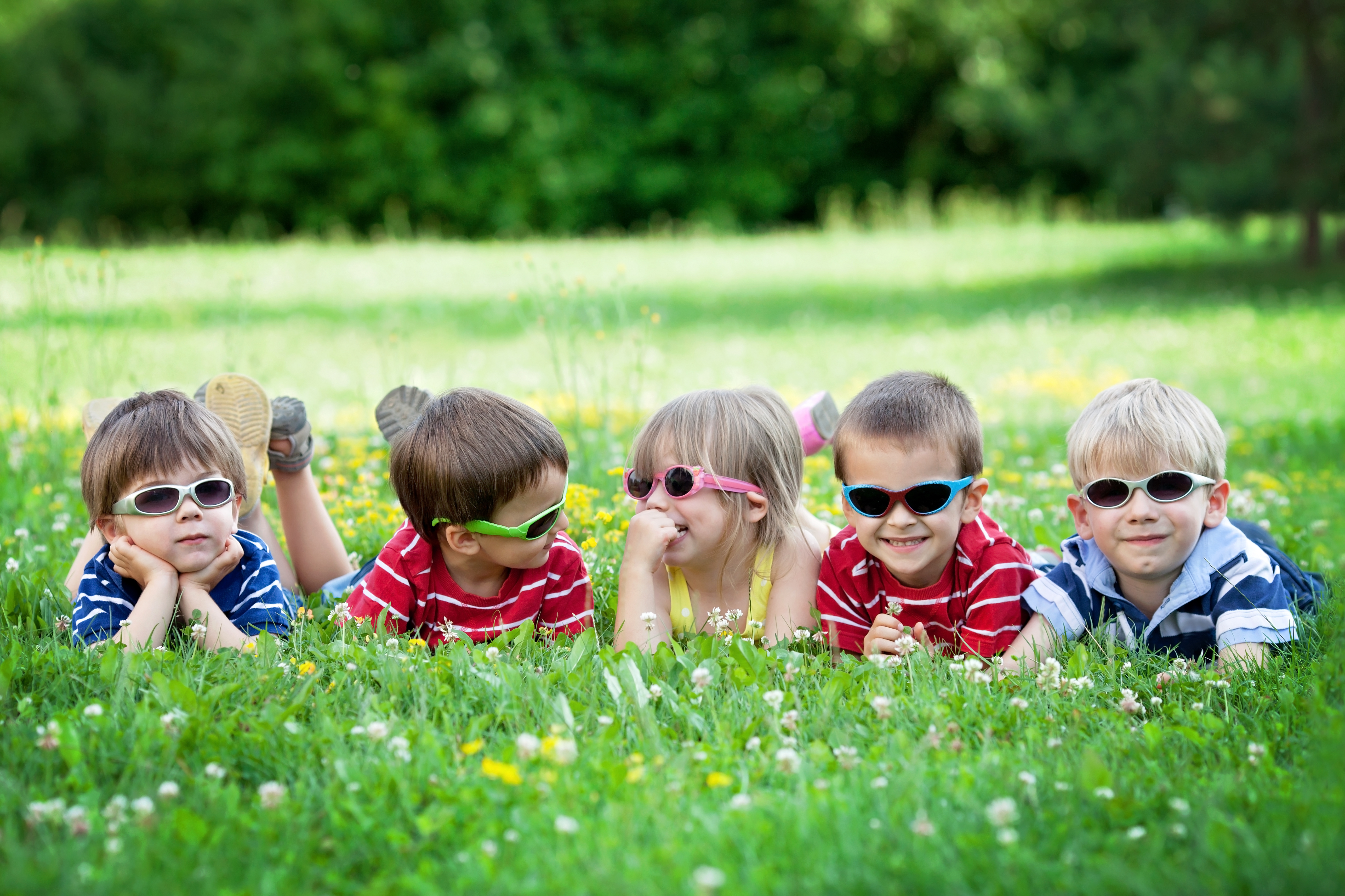 Five adorable kids, lying on the grass, smiling, having fun, wearing glasses